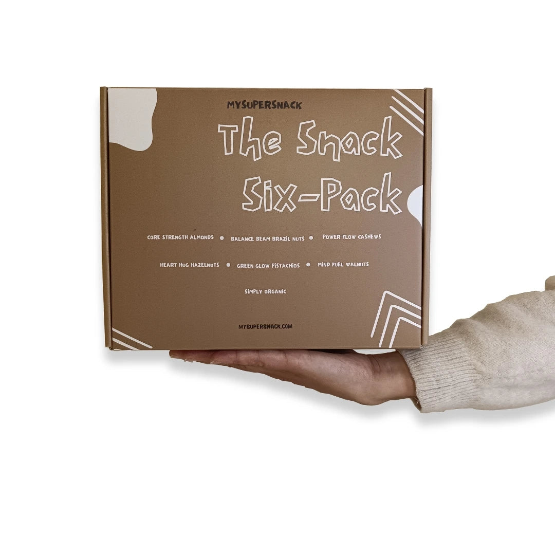 Hand holding a brown box labeled 'The Snack Six-Pack' with visible branding.